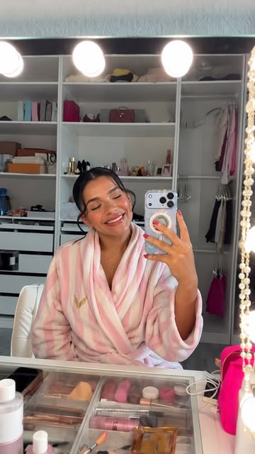 Alex Ficka at her vanity in a silk robe, holding a phone and smiling in the mirror